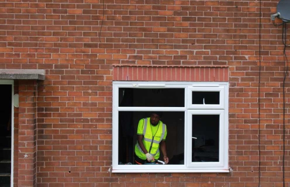 Operative in a high visibility vest working through a newly fitted white window in a red brick house
