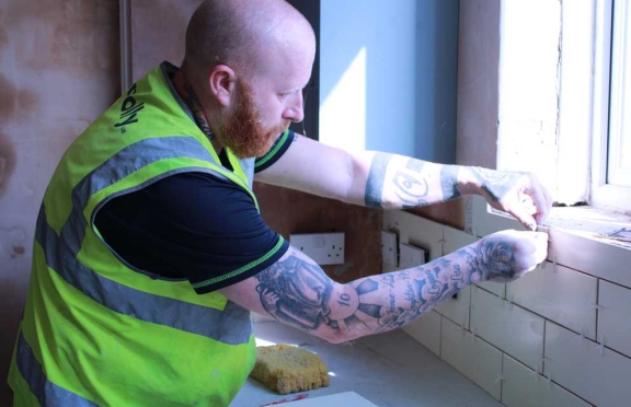 A Connolly tiler fitting wall tiles around a kitchen window