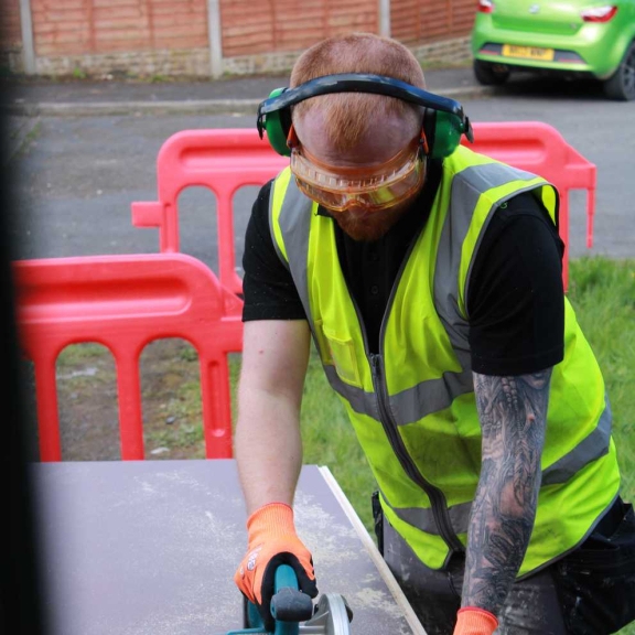 A Connolly tradesperson cutting a panel with a circular saw outdoors