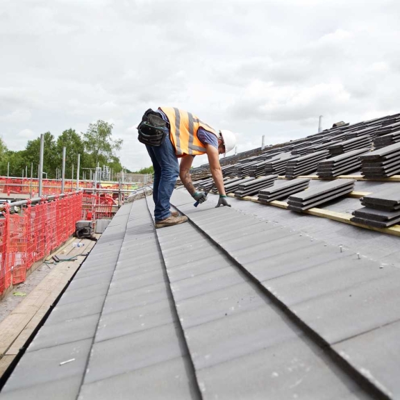 A roofer installing metal roofing panels during refurbishment projects stock