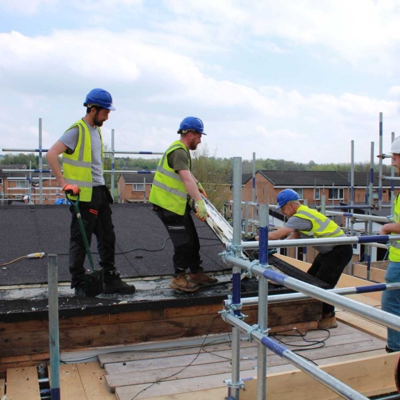 A roofing team working on a scaffolded residential block