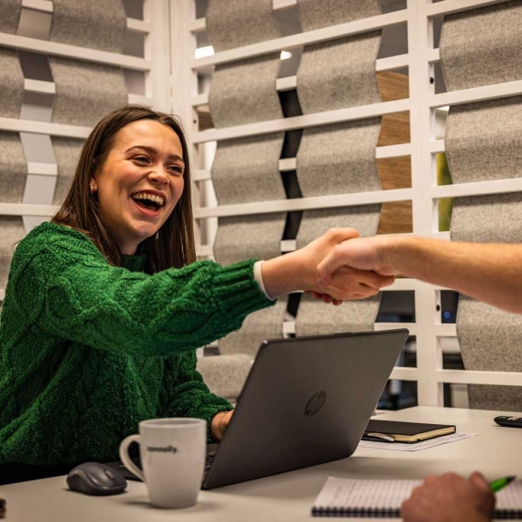 A smiling office colleague greeting another person across a laptop people offices Connolly office