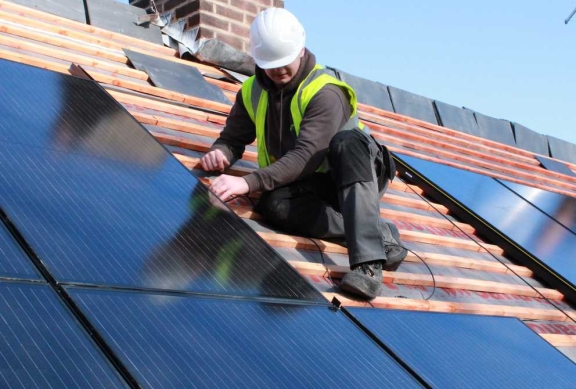 A solar installer fitting photovoltaic panels on a residential roof